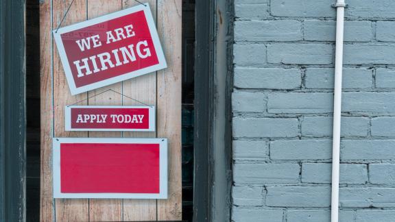 'we are hiring' sign hanging on a red wall.